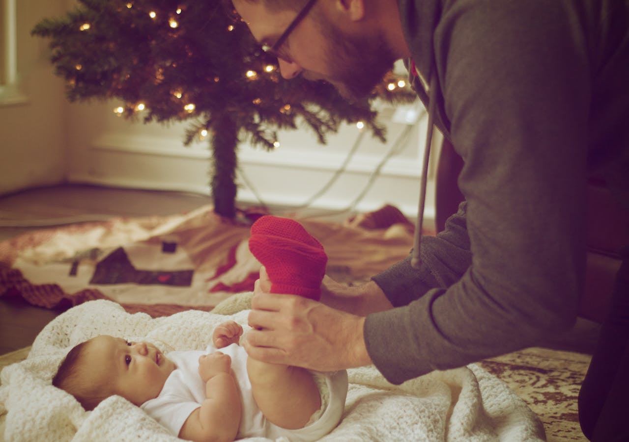 A loving father plays with his newborn near a festive Christmas tree indoors.
